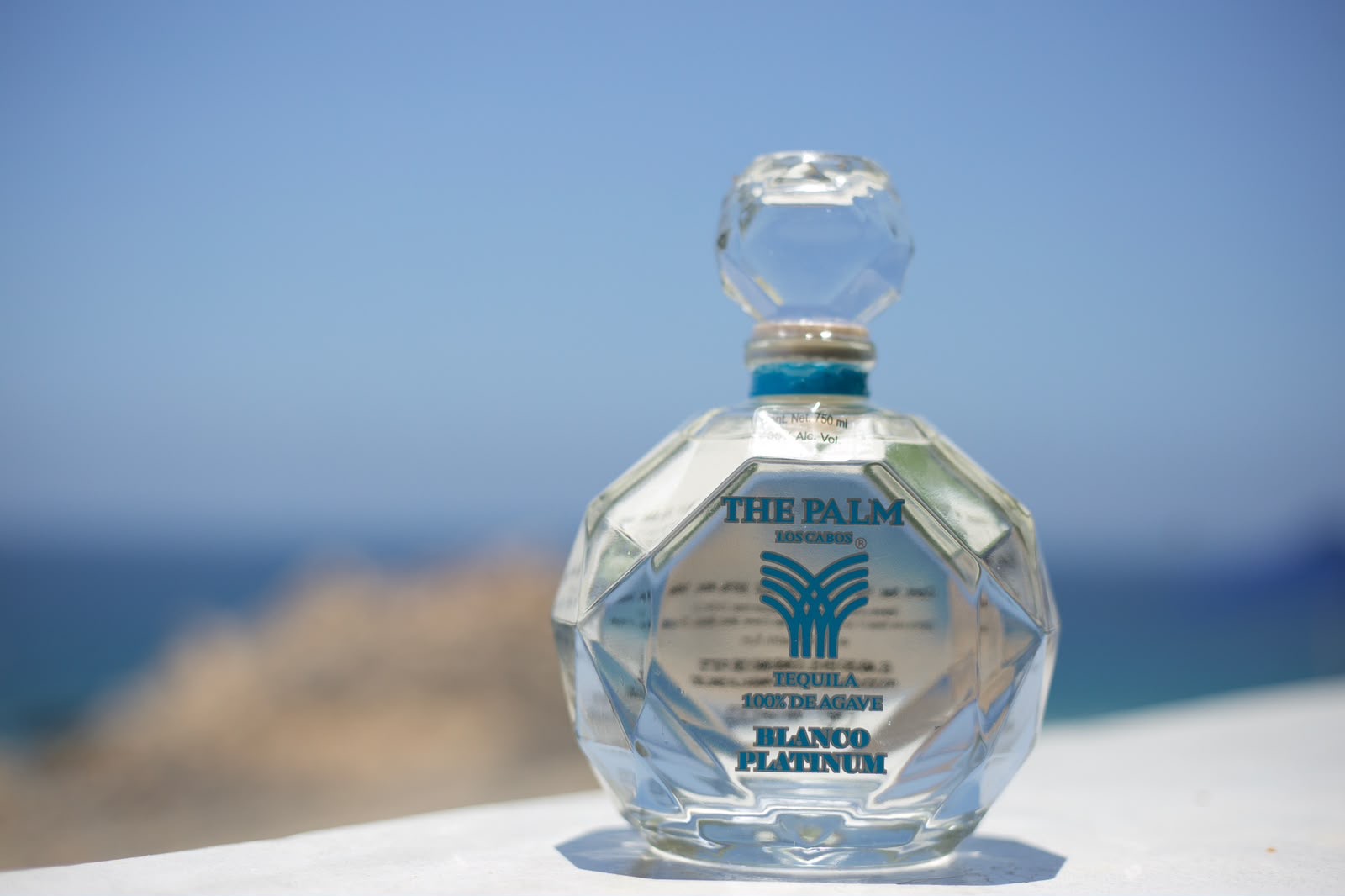The Palm Los Cabos Blanco Platinum tequila bottle with the ocean behind it